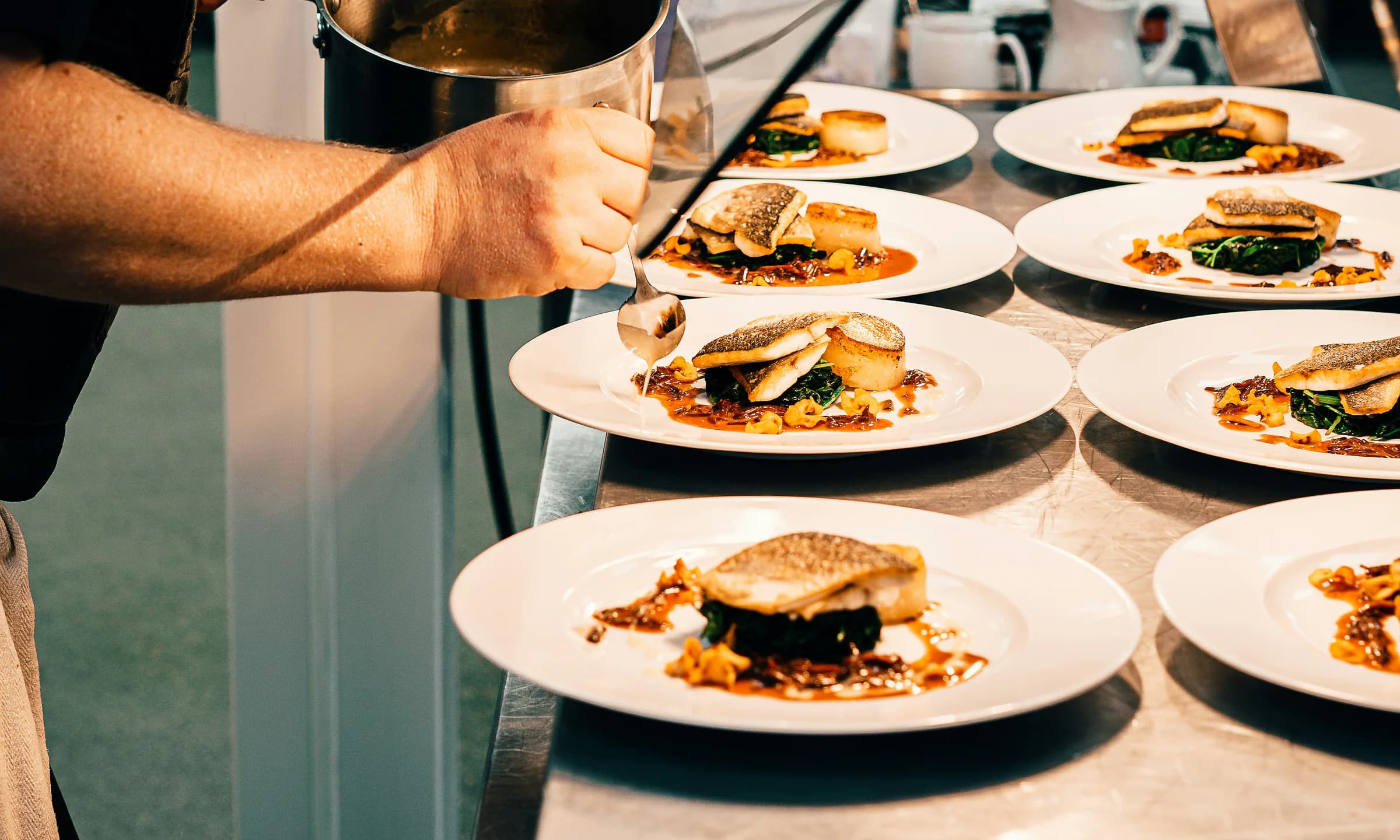 A chef finishing several plates at a restaurant kitchen pass