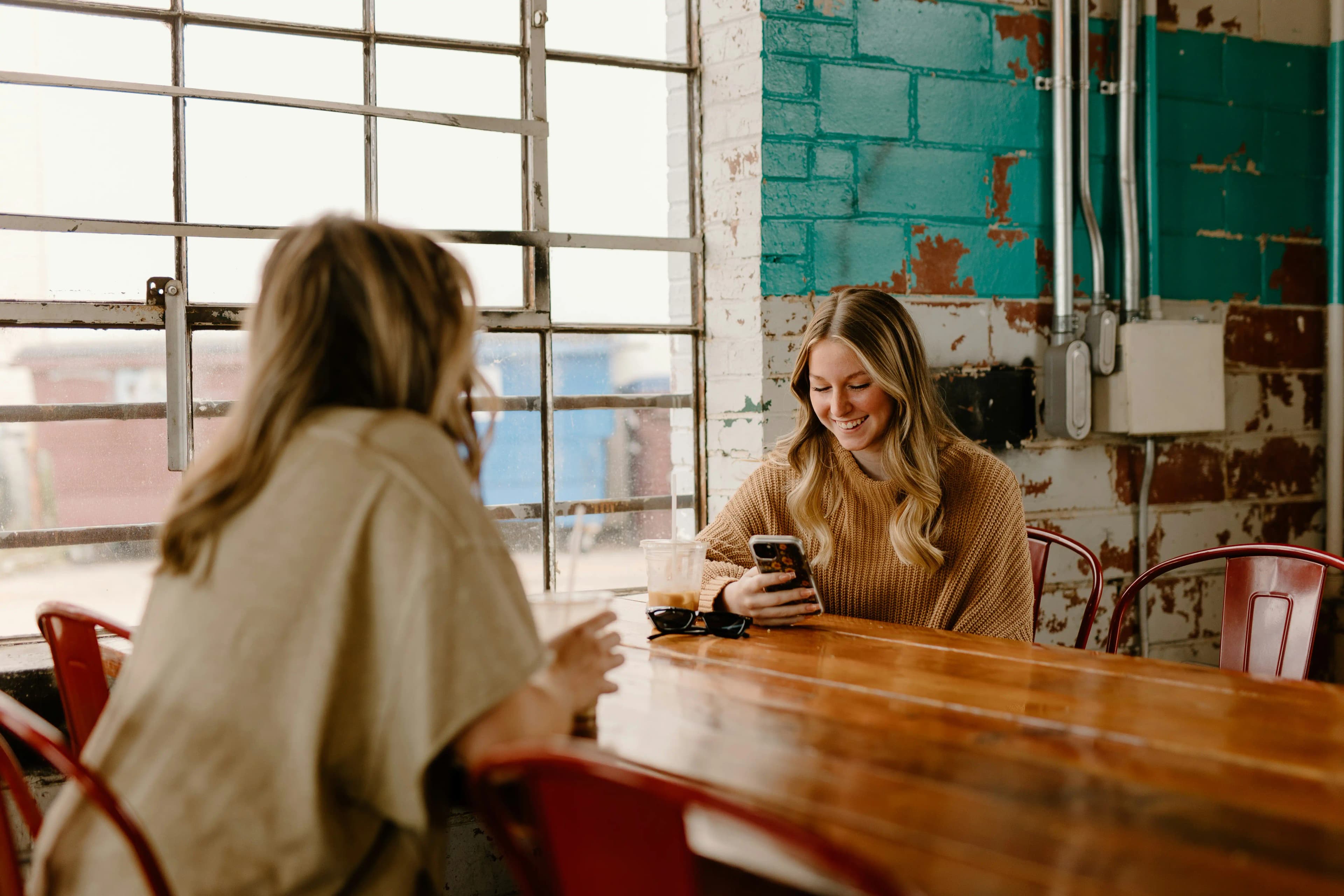 Two friends at a cafe table, one checking rewards on her phone